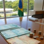 Documento oficial do Governo Lula com notas de real simbolizando salário mínimo de R$ 1.621 a partir de 2026, em escritório em Brasília.