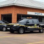 Fachada de supermercado em Iporá, Goiás, com fita de isolamento policial e viatura da PM, representando cena de crime sem pessoas.
