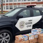 Viatura da polícia em frente a escola em Anápolis, com caixas de merenda escolar, representando suspeita de desvio.