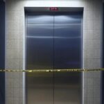Elevador em prédio de Goiânia com fita de isolamento policial, representando suspeita de crime.