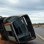 Ônibus tombado na BR-153 próximo a Interlândia, com veículos de emergência ao fundo, em paisagem rural brasileira.
