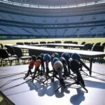 Sala de coletiva de imprensa em estádio brasileiro com mesa de microfones e atmosfera tensa, representando irritação de técnico de futebol.