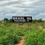 Fronteira Brasil-Venezuela em Pacaraima, com placa de divisa e vegetação amazônica, representando preocupação com eventos na Venezuela.