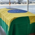 Caixão com bandeira brasileira em aeroporto, representando translado de corpo de brasileiro morto em Paris por complicações estomacais.