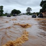 Rua inundada por enxurrada em Caldas Novas, Goiás, com água correndo e carros submersos, ilustrando tragédia por chuvas fortes.