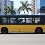 Ônibus urbano em Goiânia transportando moto no interior, cena de rua com arquitetura local.