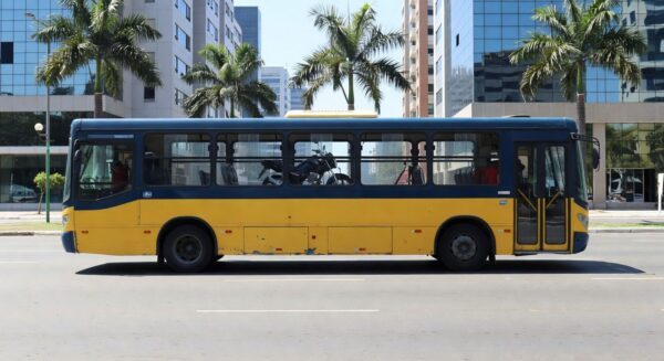 Ônibus urbano em Goiânia transportando moto no interior, cena de rua com arquitetura local.