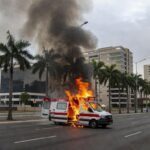 Ambulância da SOS Vida em chamas em avenida de Goiânia, com fumaça e fogo, estilo fotojornalístico.