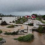 Área alagada por tromba d'água em Goiás com viaturas dos bombeiros ao fundo, representando cena de resgate após tragédia.